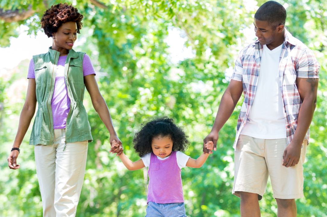 mom and dad walk hand-in-hand with little girl in park